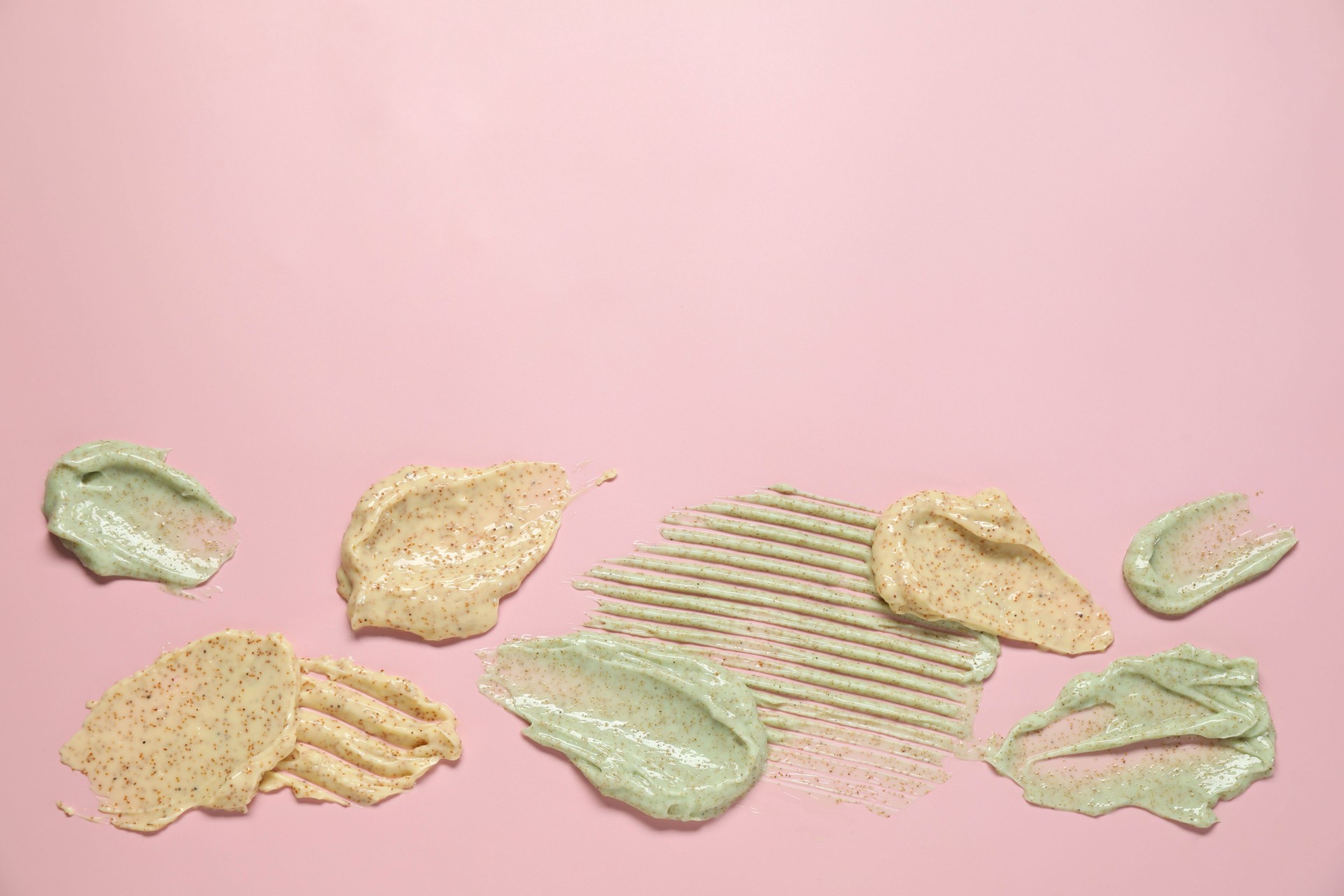 Samples of different body scrubs on pink background, top view. Space for text